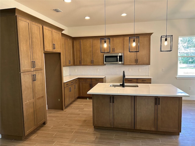 kitchen with tasteful backsplash, an island with sink, sink, and hanging light fixtures