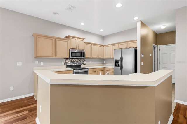 kitchen with light brown cabinetry, appliances with stainless steel finishes, light hardwood / wood-style flooring, and decorative backsplash