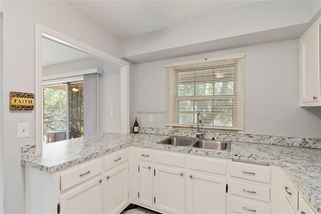 kitchen featuring a textured ceiling, sink, kitchen peninsula, and white cabinetry