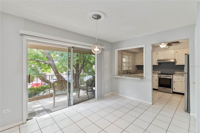 kitchen with appliances with stainless steel finishes, hanging light fixtures, light stone counters, light tile patterned floors, and ceiling fan