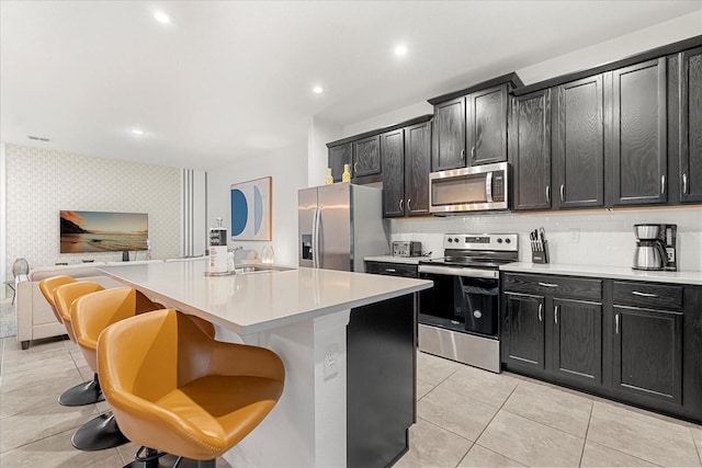 kitchen featuring decorative backsplash, a center island with sink, light tile patterned floors, a kitchen breakfast bar, and stainless steel appliances