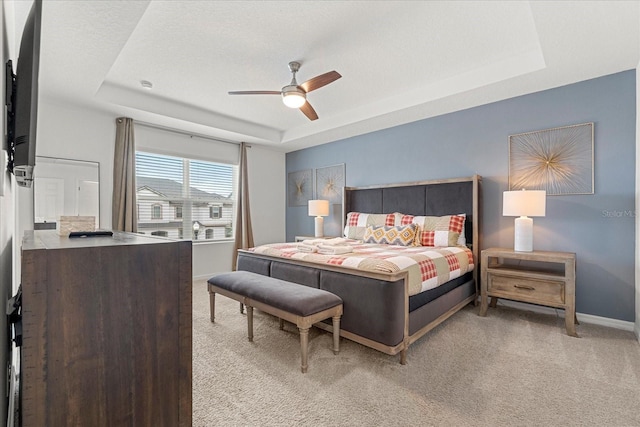 bedroom with light carpet, ceiling fan, and a raised ceiling