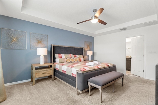 carpeted bedroom featuring ensuite bathroom, a raised ceiling, and ceiling fan