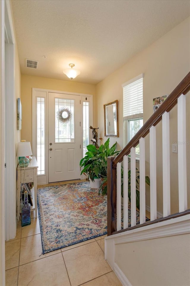 entrance foyer featuring stairway, visible vents, a healthy amount of sunlight, and tile patterned floors