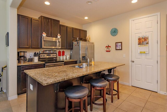 kitchen featuring a kitchen breakfast bar, stainless steel appliances, dark brown cabinetry, a center island with sink, and sink