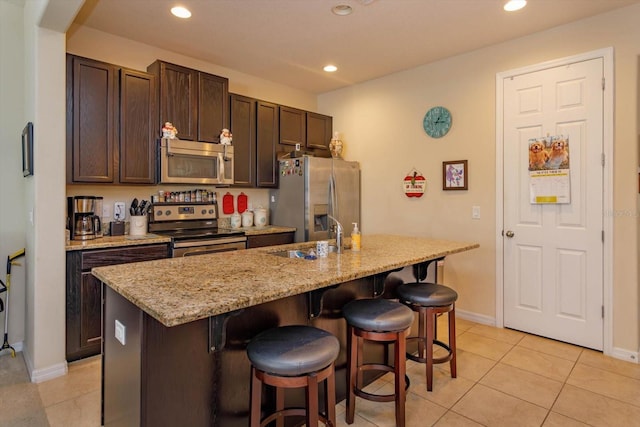 kitchen with a breakfast bar area, stainless steel appliances, a sink, an island with sink, and dark brown cabinets