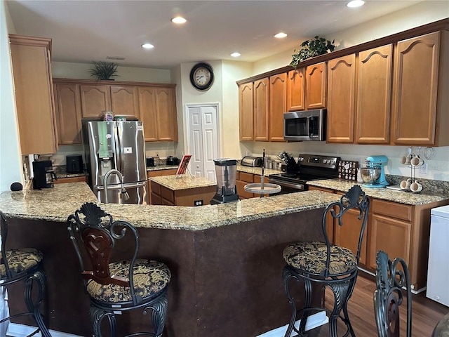 kitchen featuring a breakfast bar area, dark hardwood / wood-style flooring, stainless steel appliances, and light stone counters