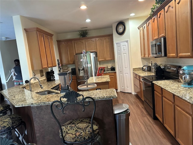 kitchen with wood-type flooring, light stone counters, sink, kitchen peninsula, and stainless steel appliances