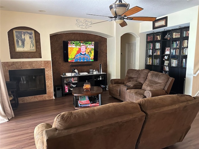 living room with ceiling fan, a tile fireplace, hardwood / wood-style flooring, and a textured ceiling