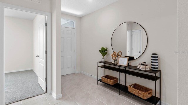 foyer entrance with light tile patterned floors, baseboards, and light colored carpet