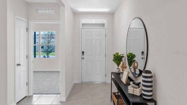 entryway featuring light tile patterned flooring, light carpet, a textured ceiling, baseboards, and visible vents