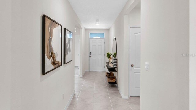 corridor featuring light tile patterned flooring, baseboards, and a textured ceiling
