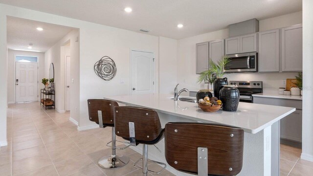 kitchen featuring light countertops, gray cabinetry, a breakfast bar, a kitchen island with sink, and appliances with stainless steel finishes