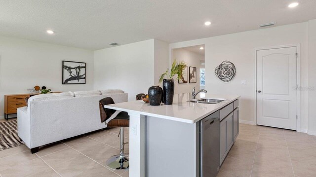 kitchen featuring light countertops, a breakfast bar area, stainless steel dishwasher, a sink, and visible vents