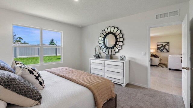 bedroom with a textured ceiling, visible vents, baseboards, light tile patterned floors, and light colored carpet