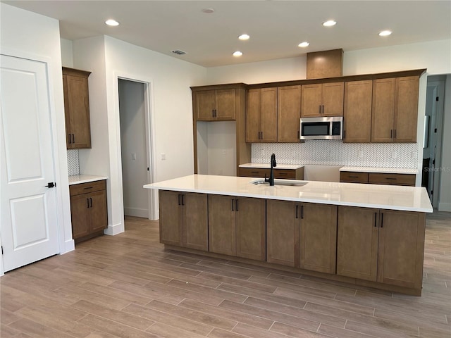 kitchen with tasteful backsplash, sink, a center island with sink, and light wood-type flooring