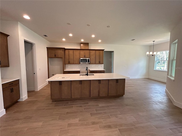 kitchen featuring tasteful backsplash, wood-type flooring, sink, a kitchen island with sink, and a notable chandelier