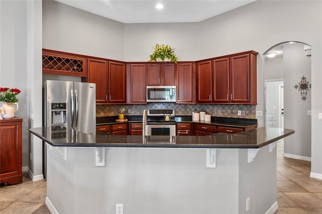 kitchen featuring a kitchen breakfast bar, stainless steel appliances, light tile patterned floors, and dark stone countertops