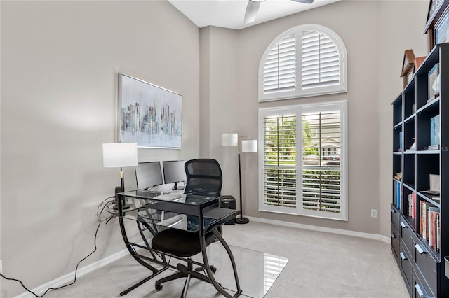 office space featuring light carpet, a towering ceiling, ceiling fan, and a healthy amount of sunlight