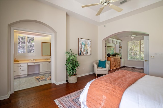 bedroom with ensuite bath, dark wood-type flooring, built in desk, and ceiling fan