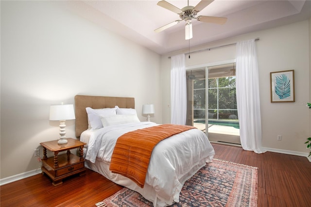 bedroom with dark wood-type flooring, ceiling fan, a raised ceiling, and access to outside