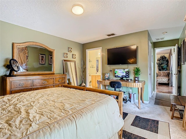 bedroom with a textured ceiling, light colored carpet, and ensuite bathroom