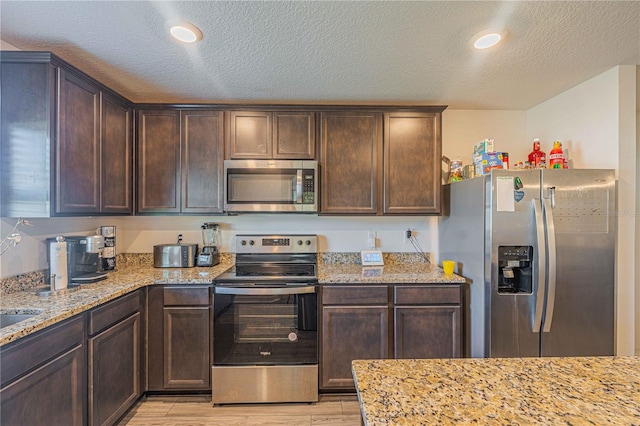 kitchen featuring appliances with stainless steel finishes, a textured ceiling, light wood-type flooring, and light stone countertops