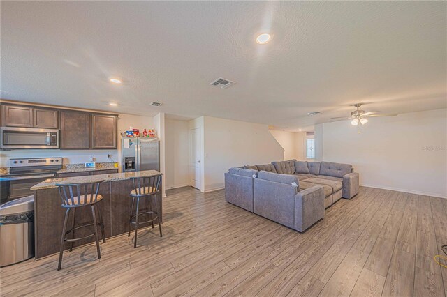 living room featuring ceiling fan, a textured ceiling, and light hardwood / wood-style floors