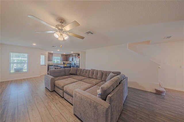 living room with light wood-type flooring, a textured ceiling, and ceiling fan