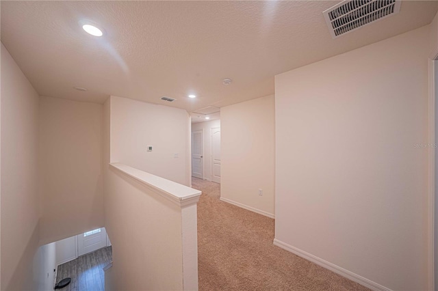 corridor featuring a textured ceiling and light colored carpet