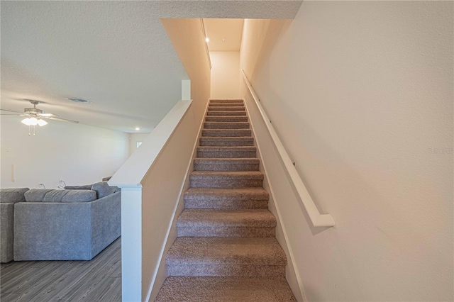 stairway featuring a textured ceiling, wood-type flooring, and ceiling fan