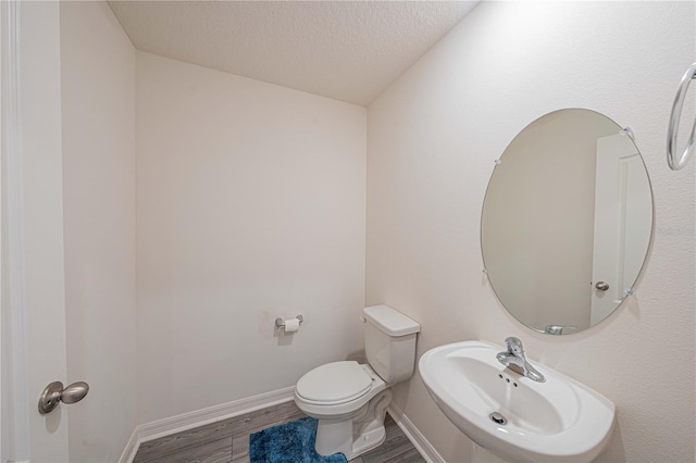 bathroom with hardwood / wood-style flooring, sink, toilet, and a textured ceiling