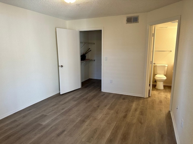 unfurnished bedroom featuring connected bathroom, a walk in closet, a closet, and dark hardwood / wood-style floors