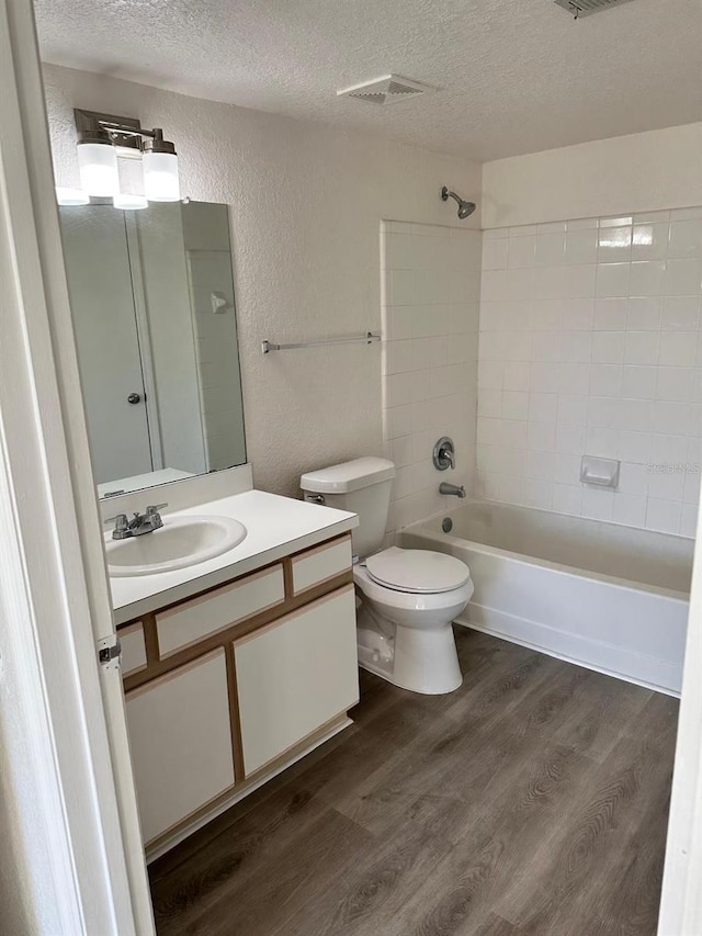 full bathroom featuring vanity, tiled shower / bath combo, toilet, a textured ceiling, and wood-type flooring