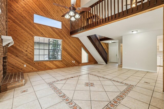 unfurnished living room with light tile patterned flooring, wood walls, a high ceiling, ceiling fan, and a skylight