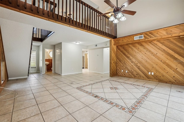 unfurnished living room featuring a high ceiling, light tile patterned flooring, wooden walls, and ceiling fan