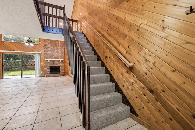 stairs featuring wooden walls, ceiling fan, a large fireplace, and tile patterned floors