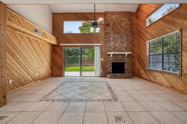 unfurnished living room featuring ceiling fan, a skylight, wood walls, light tile patterned floors, and high vaulted ceiling