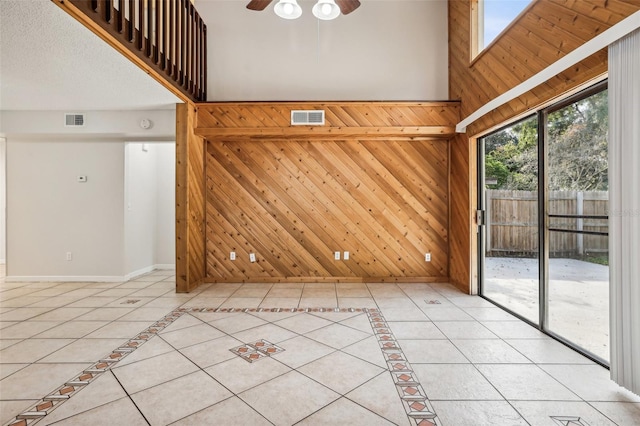 spare room with ceiling fan, light tile patterned floors, a textured ceiling, wooden walls, and a high ceiling