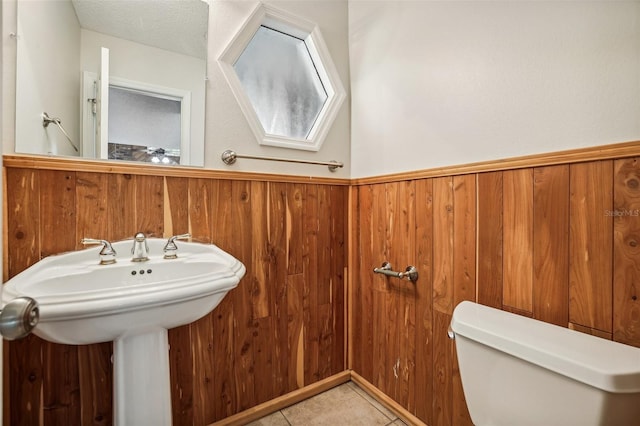 bathroom with tile patterned flooring, wood walls, a textured ceiling, and toilet