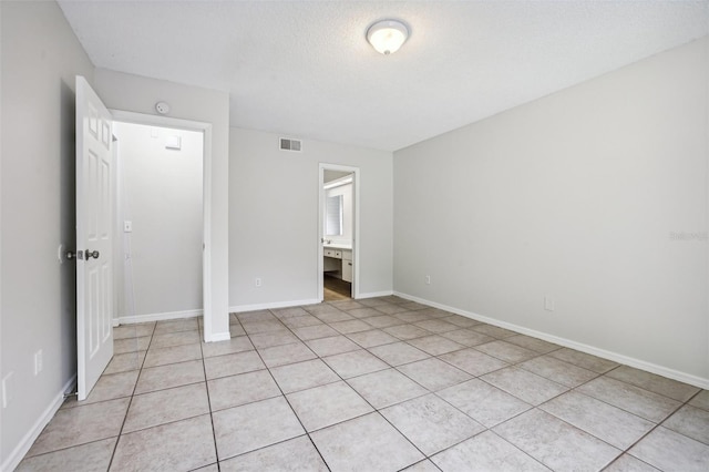 unfurnished bedroom featuring a textured ceiling, ensuite bathroom, and light tile patterned flooring