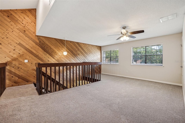 unfurnished room with a textured ceiling, carpet, wooden walls, and ceiling fan