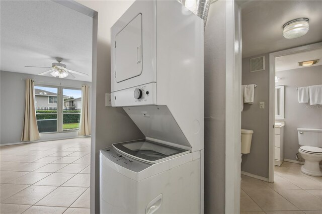 washroom featuring stacked washer and dryer, ceiling fan, and light tile patterned floors