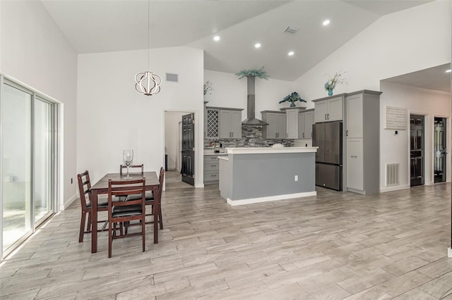 kitchen with stainless steel fridge, light hardwood / wood-style flooring, high vaulted ceiling, wall chimney range hood, and gray cabinets