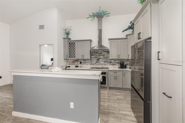 kitchen with gray cabinetry, wall chimney range hood, and an island with sink