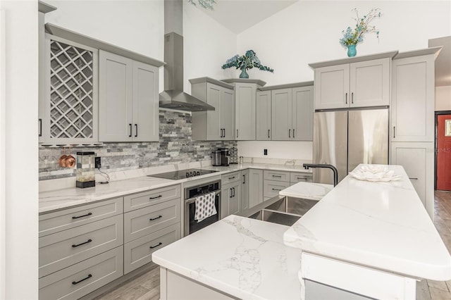 kitchen featuring appliances with stainless steel finishes, light hardwood / wood-style floors, gray cabinets, a center island, and wall chimney range hood