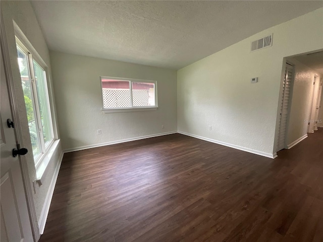 empty room featuring a textured ceiling, dark hardwood / wood-style flooring, and plenty of natural light