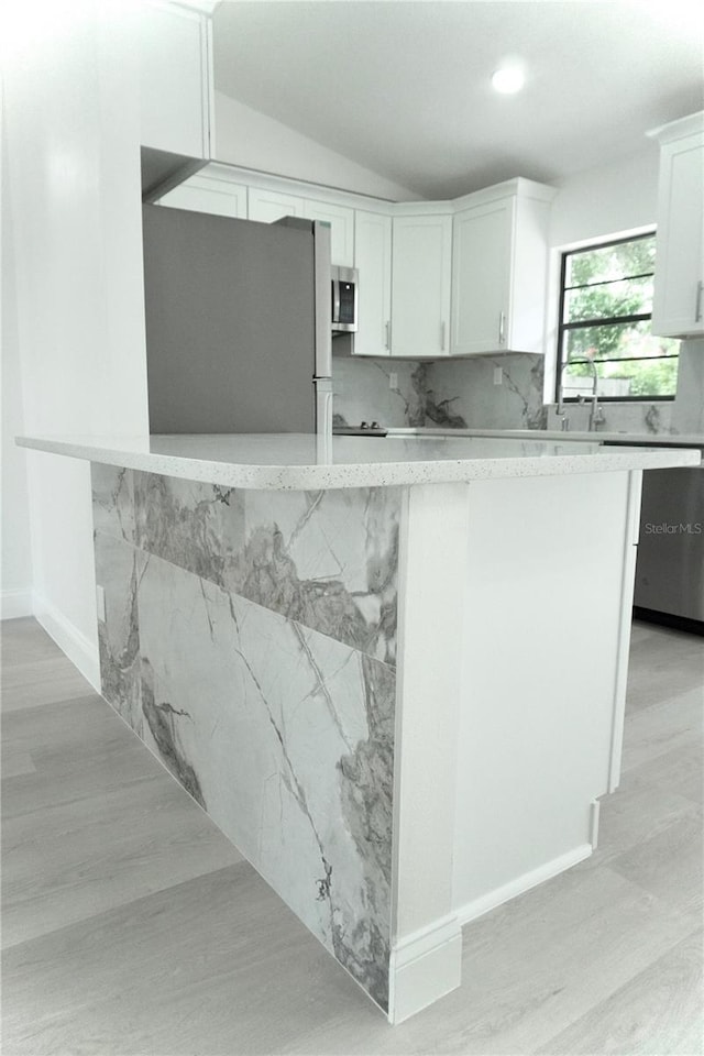 kitchen featuring appliances with stainless steel finishes, white cabinetry, backsplash, lofted ceiling, and light hardwood / wood-style flooring