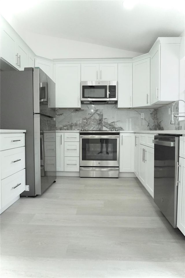 kitchen featuring stainless steel appliances, vaulted ceiling, and white cabinetry