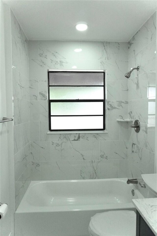 full bathroom featuring tiled shower / bath, vanity, toilet, and plenty of natural light